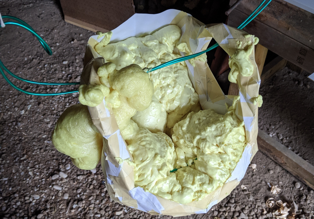 Suspended from a loop of green wire in a gravel-floored shed, the head has been filled with spray foam.