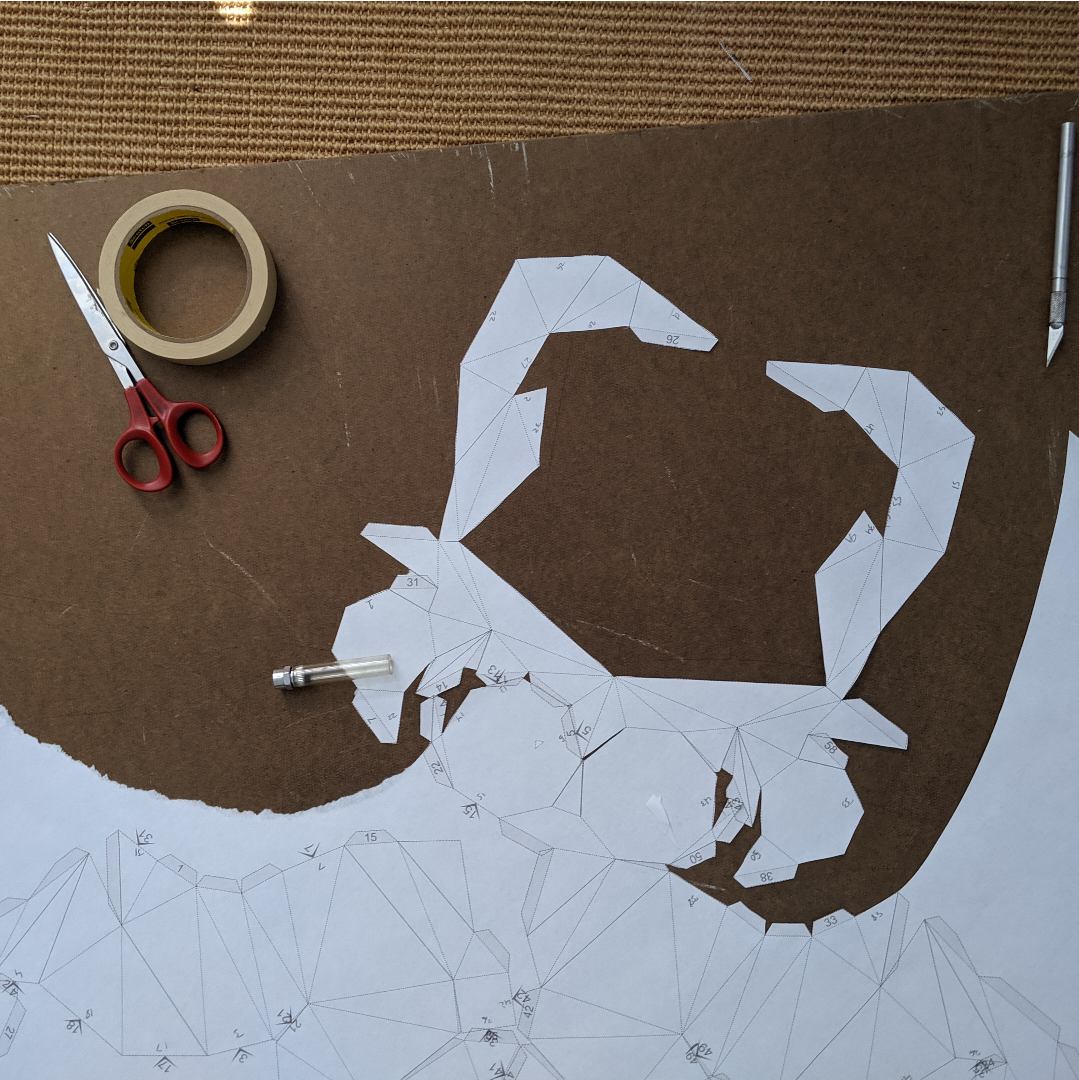 Against a brown board, slowly trimming the polygons out from the surrounding blank paper.