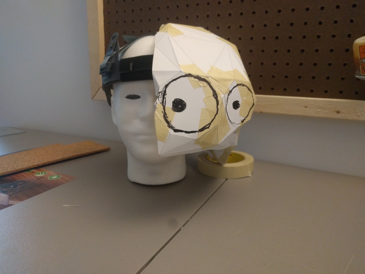 A papercraft head is displayed, split in half vertically, positioned on a styrofoam head.