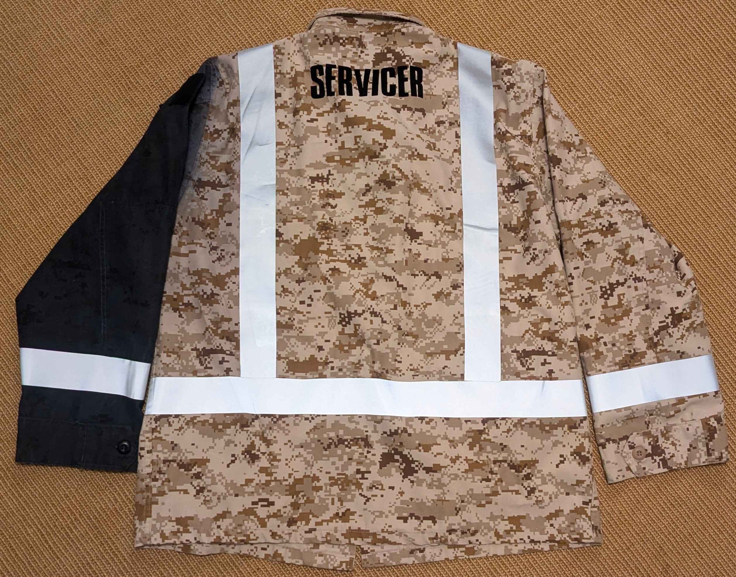 a desert camo coat lies flat on the floor. retroreflective tape makes bands around the sleeves, in a stripe around the waist, and in stripes running over each shoulder.